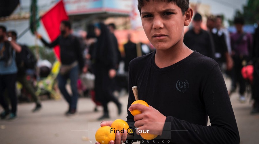 پسر بچه در حال دادن میوه به زائرام کربلا و امام حسین